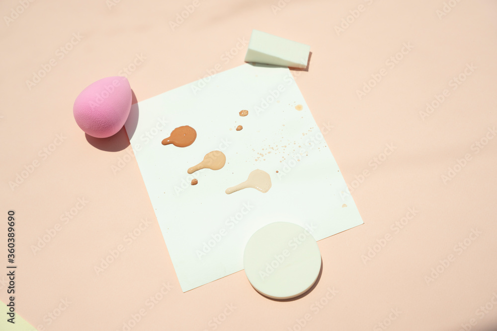 Powder puff sponge and liquid cosmetic on testing paper over beige background. Powder puff sponge and liquid cosmetic on testing paper over beige background.