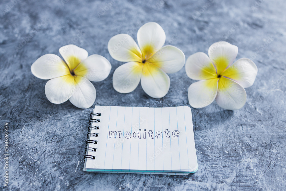 mental health concept, notepad with text Meditate next to tropical flowers on grey concrete surface mental health concept, notepad with text Meditate next to tropical flowers on grey concrete surface