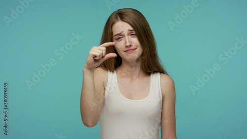 Cute positive girl looking at camera with disappointed pitiful expression and showing a little bit gesture, feeling skeptical about small size, low scale. studio shot isolated on blue background