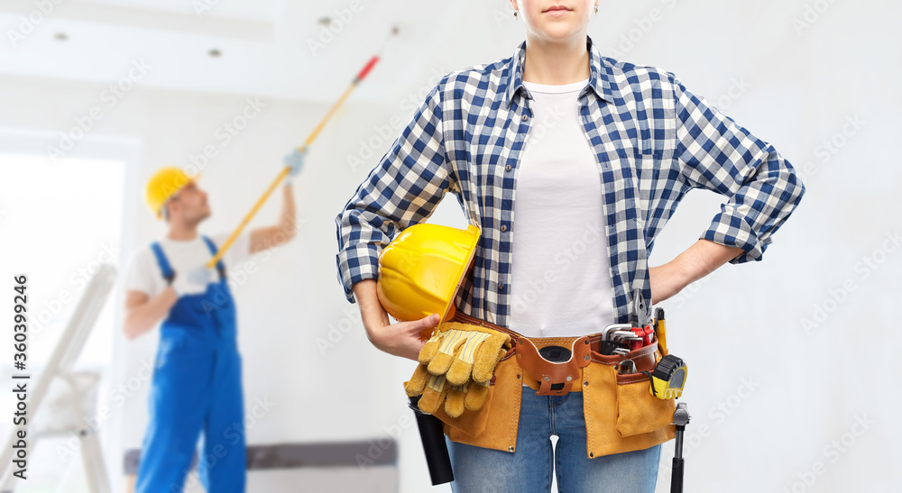 repair, construction and building concept - woman or builder with helmet and working tools on belt over painter painting ceiling background
