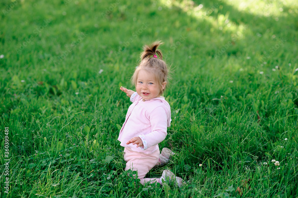 Little cute girl in casual wear sits on her knees on the green grass. Little cute girl in casual wear sits on her knees on the green grass.