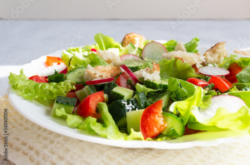 Fattoush salad of vegetables and toasted pita bread in a white plate with a napkin on a light background. Close up. Summer vegetarian salad