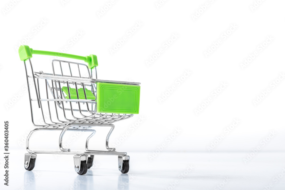 Close up of supermarket grocery push cart for shopping with black wheels and green plastic elements on white background. Concept of shopping. Copy space for advertisement.