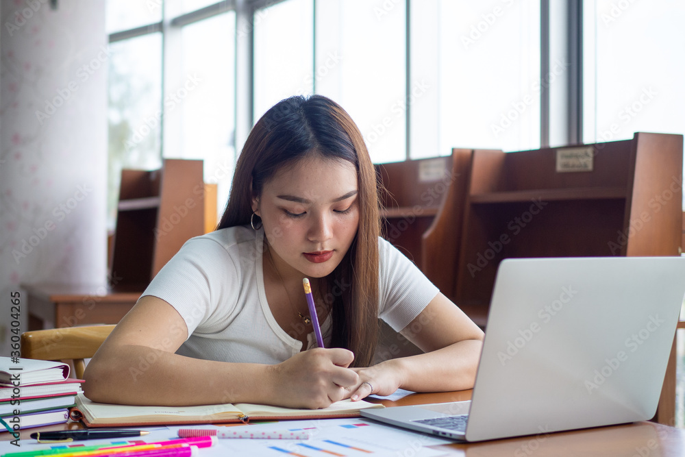 Asian female students are sitting reading books in the university library. Students prepare exams and report or study online through a computer. Asian female students are sitting reading books in the university library. Students prepare exams and report or study online through a computer.