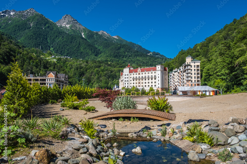 Hotel in the mountains. Rest in nature. Green trees. Lake. A wooden bridge. Resort in the mountains. Rosa Khutor. Sochi