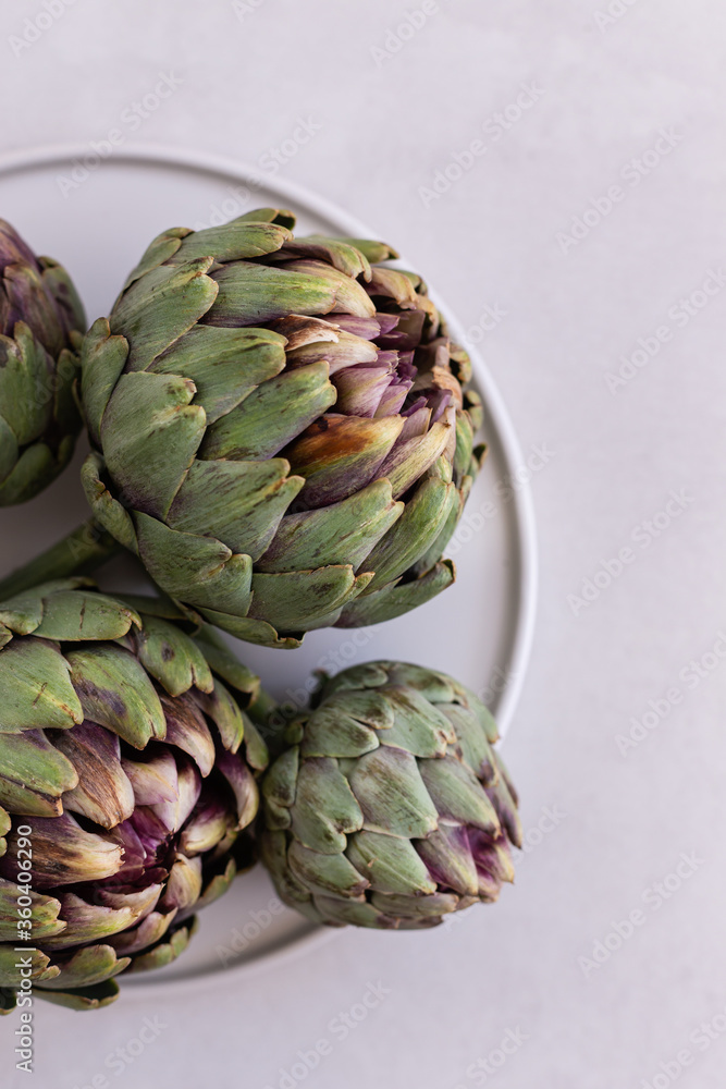 Obraz premium Topview image of artichokes in a white plate over light gray bac