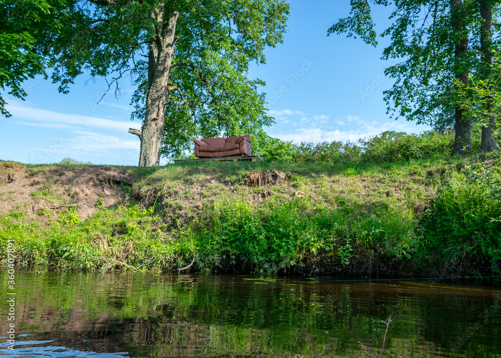 summer landscape with a small river, brown sofa on the shore, beautiful reflections in the water, summer river reflection landscape. summer landscape with a small river, brown sofa on the shore, beautiful reflections in the water, summer river reflection landscape.