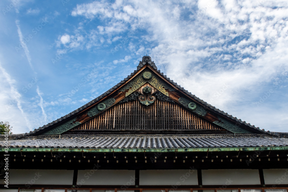Wooden, richly decorated Nijo Castle roof in Kyoto, with golden ornaments, Japan. Blue sky in the background, symmetrical view. Wooden, richly decorated Nijo Castle roof in Kyoto, with golden ornaments, Japan. Blue sky in the background, symmetrical view.