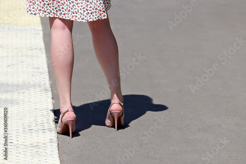 Slim female legs on high heels, woman in summer dress and high-heeled shoes standing on a street in dry sunny weather. Ladies fashion and footwear, health of the feet