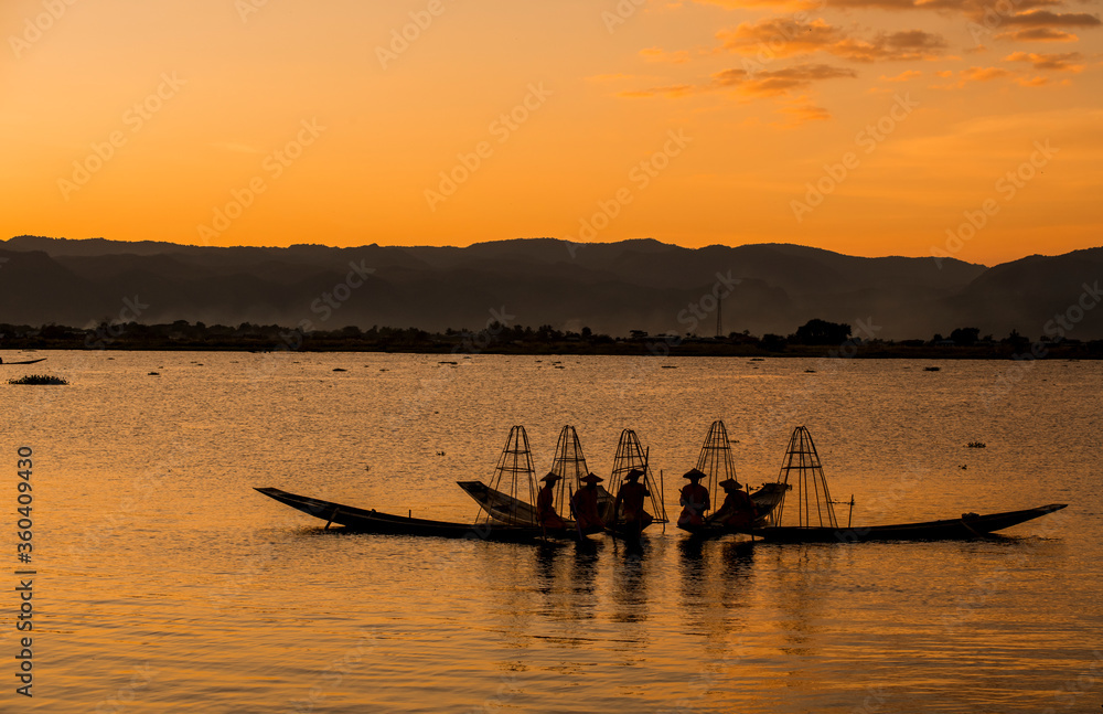 Silhouette fishermen catches fish for food in sunrise rays at Inle lake ,Myanmar .Intha people lifestyle with early morning sun sky.