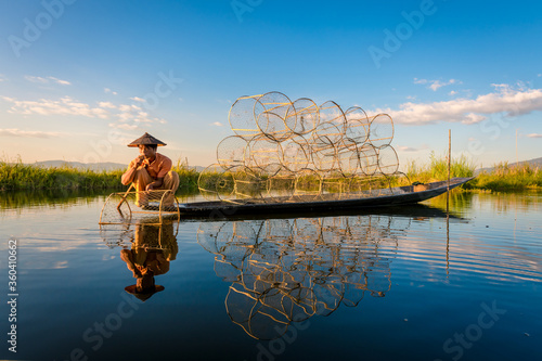 A fisherman show catches fish for food in sunrise rays at Inle lake ,Myanmar .Intha people lifestyle with blue white cloud sun sky photo