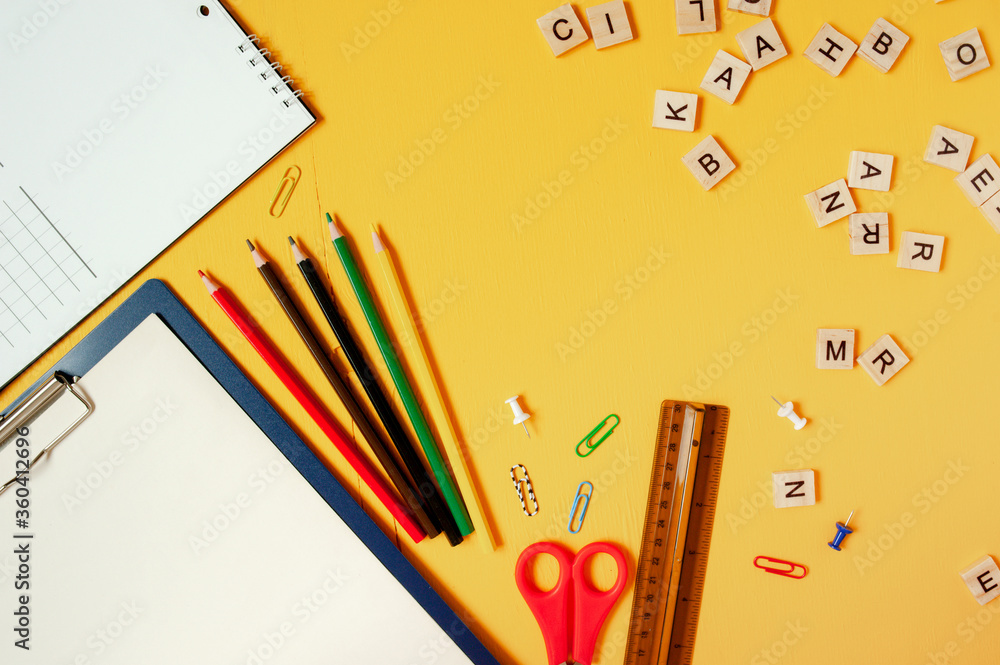 School layout, school supplies and accessories on a bright yellow background and scattered wooden letters School layout, school supplies and accessories on a bright yellow background and scattered wooden letters