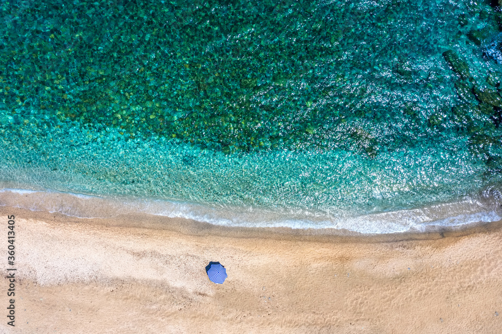 Naklejka premium An umbrella on a empty beach with emerald and turquoise sea at the Aegean Islands of Greece, Andros