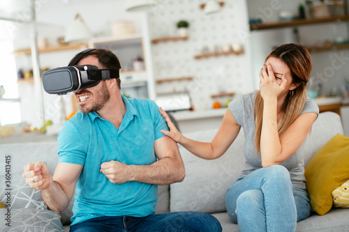Smiling young man using VR headset at home on couch. Man and his wife enjoying virtual reality at her apartment.	