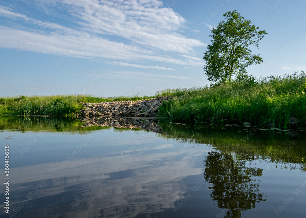 Obraz premium summer landscape, river bank pollution, concrete blocks thrown into the river, reflections in the water