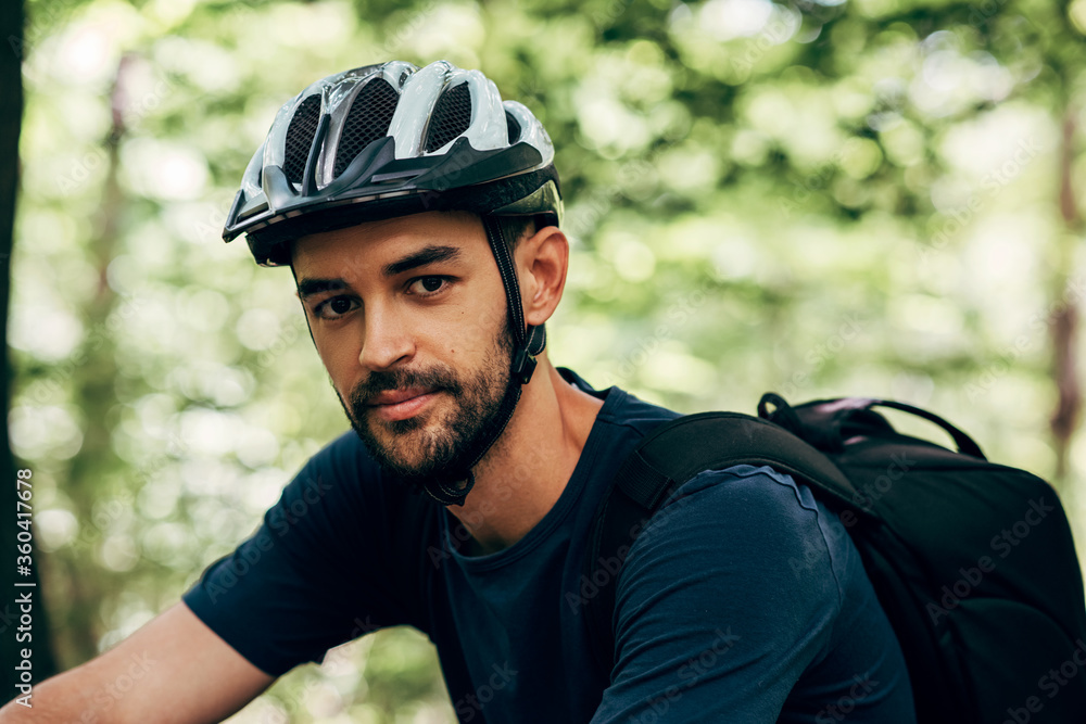 Closeup outdoor portrait of handsome cyclist man riding bike in the mountain. Smiling male athlete bicyclist in cycling gear practising outside on nature background. Travel and extreme sport concept. Closeup outdoor portrait of handsome cyclist man riding bike in the mountain. Smiling male athlete bicyclist in cycling gear practising outside on nature background. Travel and extreme sport concept.