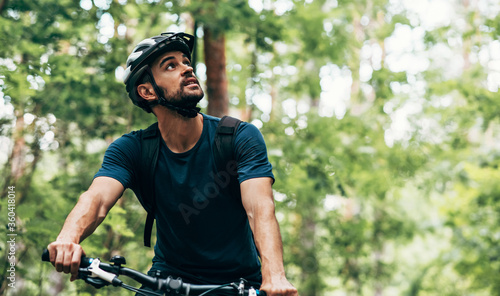 Outdoor image of handsome cyclist man riding bike in the mountain. Male athlete in cycling gear practising outside in the forest on nature background. Travel and extreme sport concept. photo