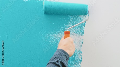 Man painting wall with blue paint using roller. Construction worker, tool, apartment renovation. photo