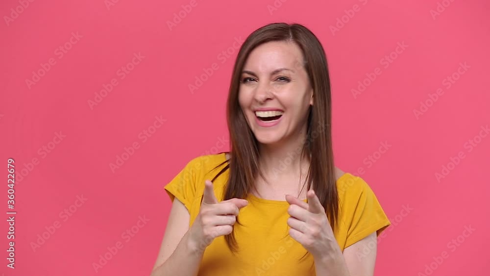 Beautiful young woman in yellow t-shirt posing isolated on pink background studio. People emotions lifestyle concept. Looking at camera with charming smile pointing fingers on you say cool approval Beautiful young woman in yellow t-shirt posing isolated on pink background studio. People emotions lifestyle concept. Looking at camera with charming smile pointing fingers on you say cool approval