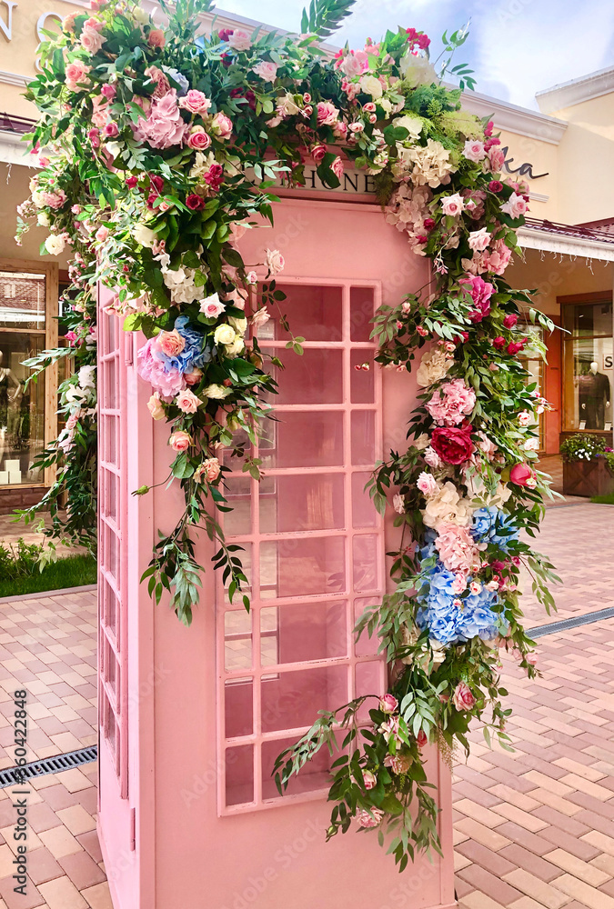 A beautiful telephone box stands on the street. Decorated with beautiful flowers roses, hydrangea, greenery. Beautiful decoration of a bouquet of flowers