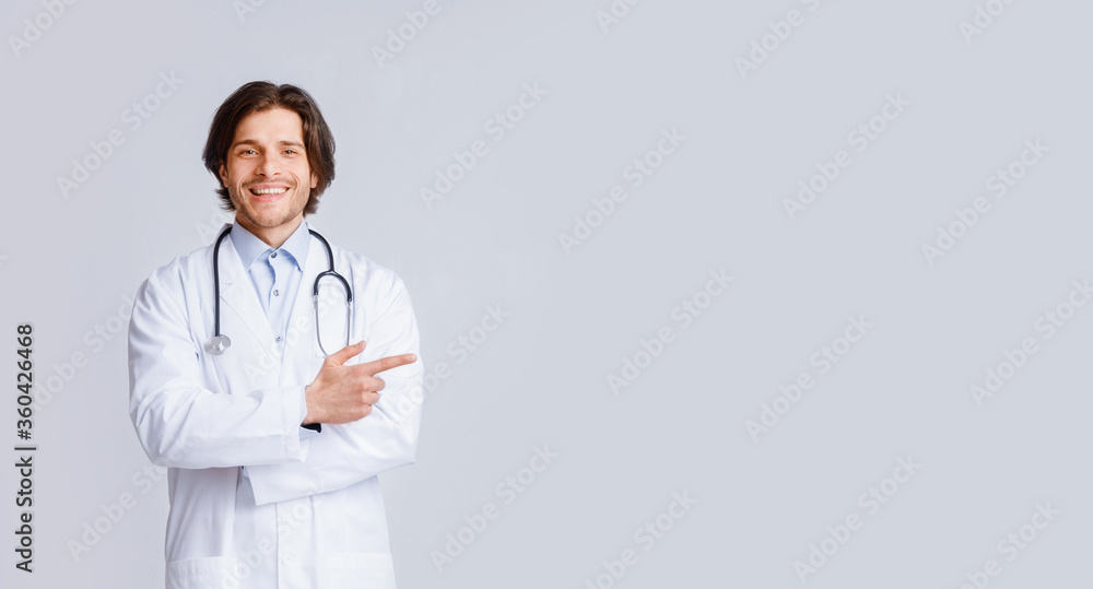 Friendly Male Doctor Therapist In White Lab Coat With Stethoscope Pointing Aside Friendly Male Doctor Therapist In White Lab Coat With Stethoscope Pointing Aside