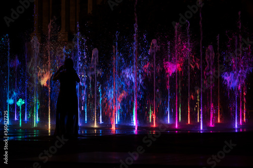 Beautiful night scene of young couple in light park, lovers silhouettes against green fountain
