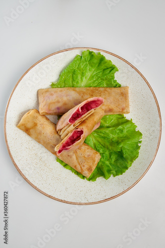 Pancakes with berry filling lie on a white plate with green salad. White background. Russian traditional cuisine.