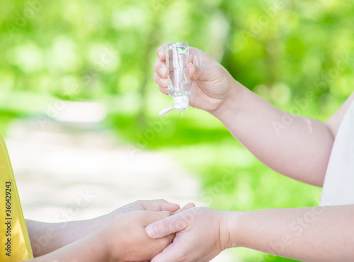 Mother applies sanitizer for cleaning son's hands in public place or summer park