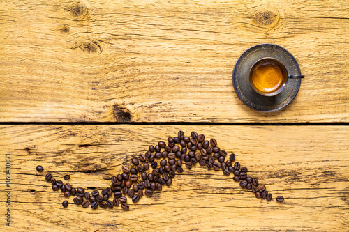 Rustic background with coffee beans arranged in a pattern and a silver espresso cup on wooden table.