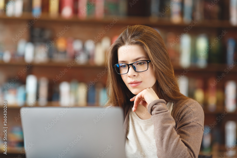 Calm young girl in eyeglasses working on laptop in cafe Calm young girl in eyeglasses working on laptop in cafe