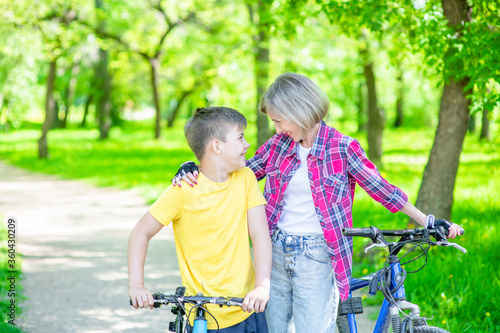 Happy family. Smiling mom hugs her young son, while they ride a bike in summer park