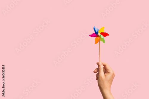 Mano de mujer sosteniendo un molinete molino de viento de colores sobre un fondo rosa liso y aislado. Vista de frente. Copy space photo