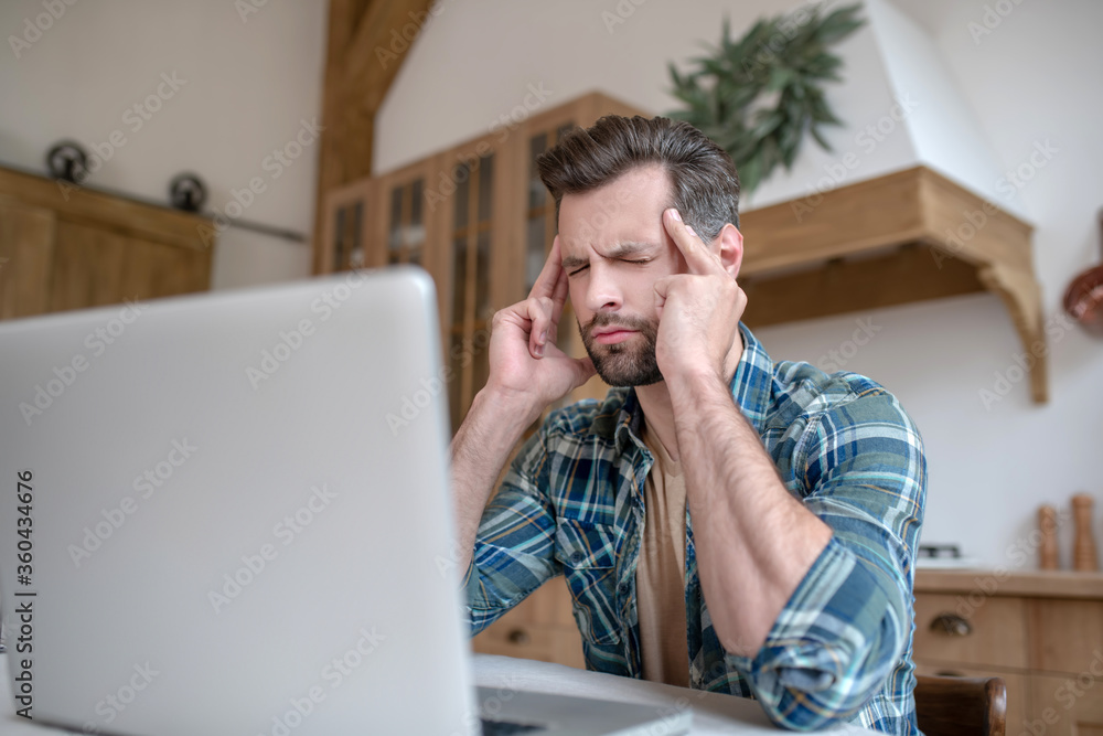 Man in a checkered shirt looking tired and suffering from headache Man in a checkered shirt looking tired and suffering from headache