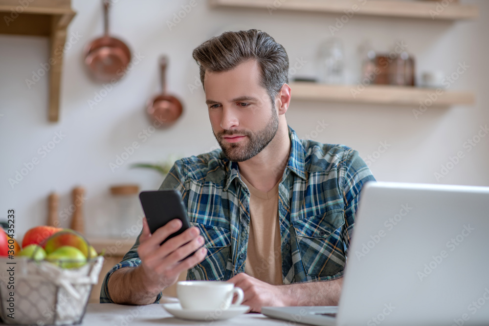 Man in a checkered shirt holding a smartphone and reading a message Man in a checkered shirt holding a smartphone and reading a message