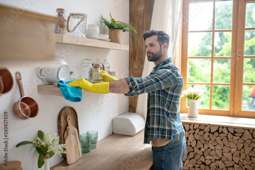 Dark-haired man in yellow gloves cleaning the kitchen and looking involved