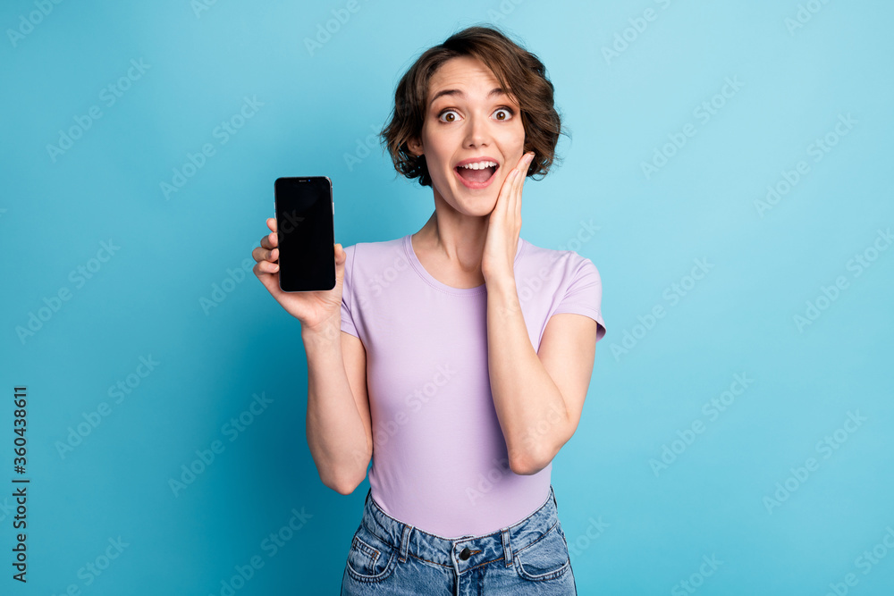 Photo of astonished positive girl hold smartphone impressed modern technology discounts touch hand face wear good look outfit isolated over blue color background Photo of astonished positive girl hold smartphone impressed modern technology discounts touch hand face wear good look outfit isolated over blue color background
