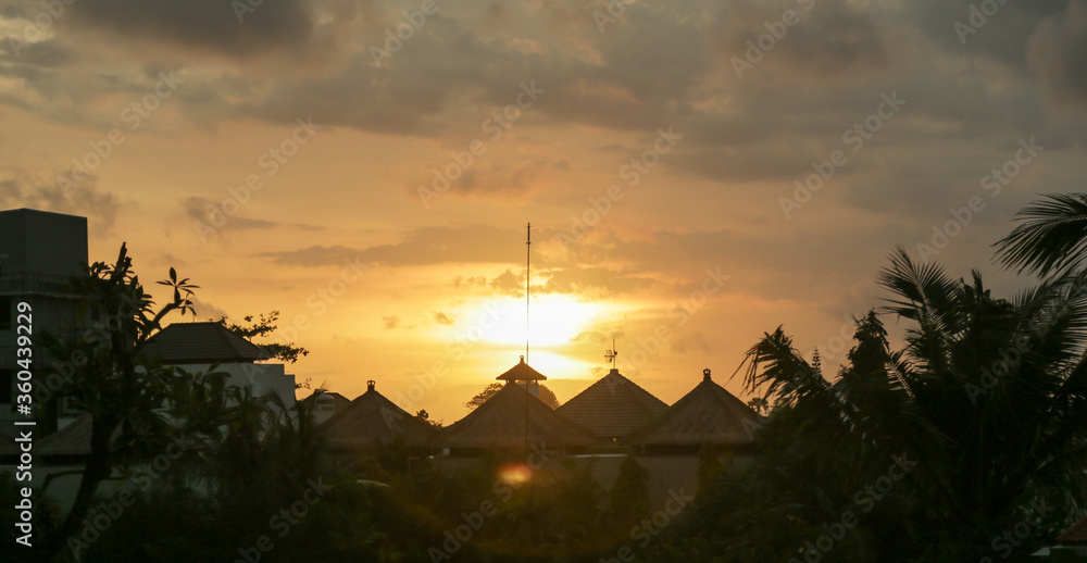 Beautiful orange sunset in bali. Local houses, palm trees, antennas, exotic plants. Summer evening shooting