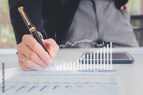 Close up hand businessman writing with pen, financial data and sales rates and market exchanges or appropriate paper reports with graphs showing business growth. Concepts of financial investment