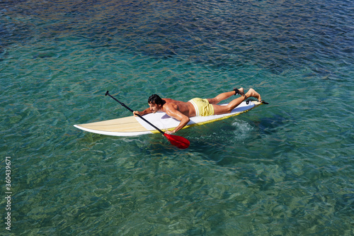 Shot of a handsome young man enjoying a surf in clear blue water, male surfer in the ocean water with surf board, sexy man surfing at the beach, men drifting on surfboard in the copy space ocean
