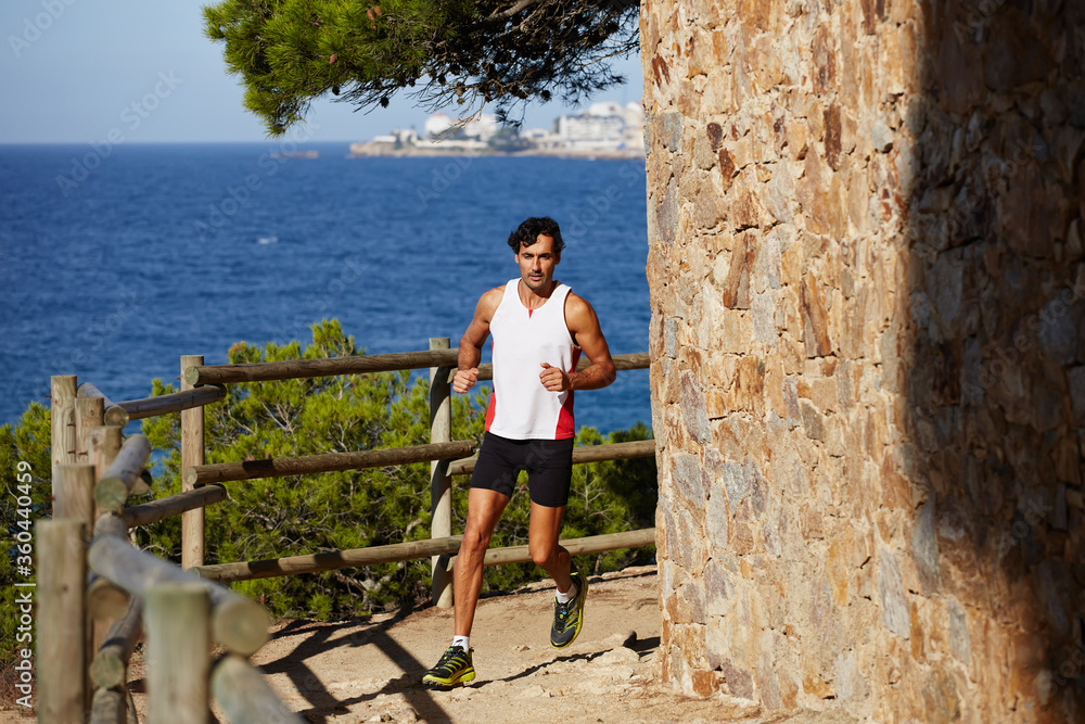 Full length portrait of a handsome young male athlete jogging outdoors with amazing sea horizon on background, jogging athlete over mountain trail on high altitude Full length portrait of a handsome young male athlete jogging outdoors with amazing sea horizon on background, jogging athlete over mountain trail on high altitude