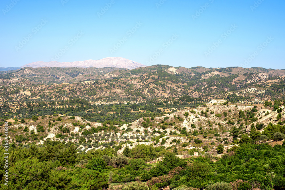 Rhodes island scenery on a sunny summer day with dry trees, fields, brown soil and blue clear sky with haze