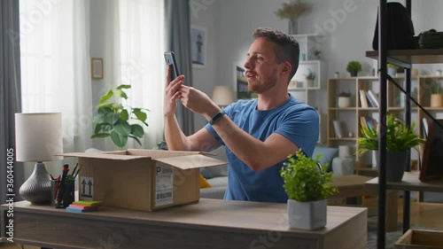 Handsome young man takes a smartphone out of a cardboard box. Unpacking online purchases.