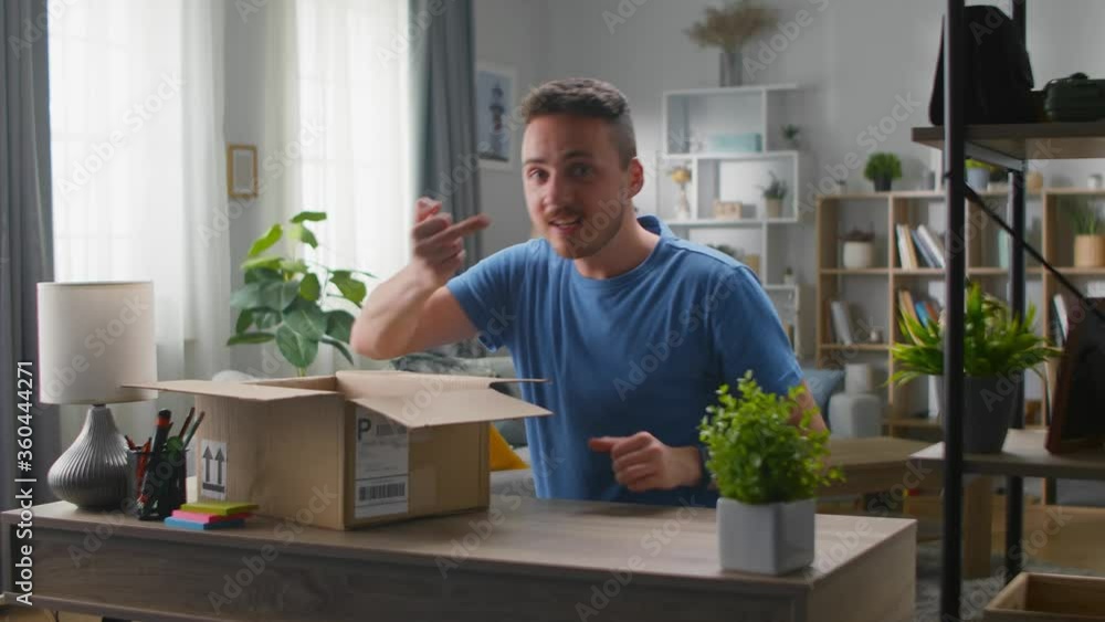 Handsome young man takes his middle finger out of a cardboard box. Unpacking online purchases. Handsome young man takes his middle finger out of a cardboard box. Unpacking online purchases.