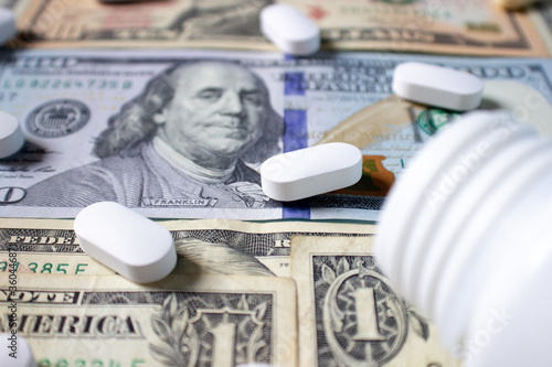 White pills and a medical bottle on one and one hundred dollar bills. Health insurance concept. Medicine and money. Medical background.
