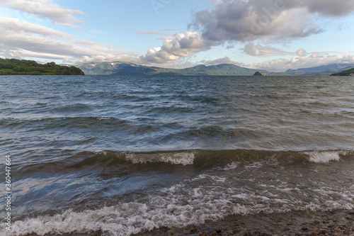 Daytime view of the lake in windy weather. With a view of the volcano on the horizon. A view from the shore of the lake with a volcano on the horizon in sunny weather.