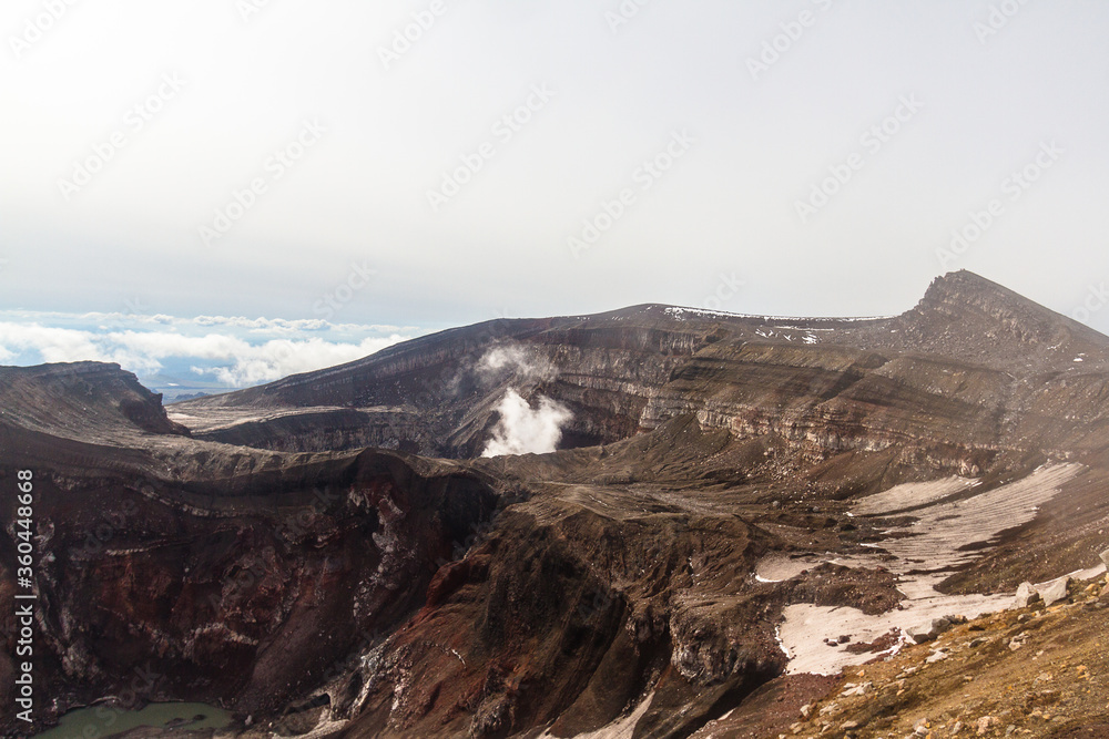Daytime view of the mouth of an active volcano. Clouds on the horizon, mountains, volcanic lake are visible.