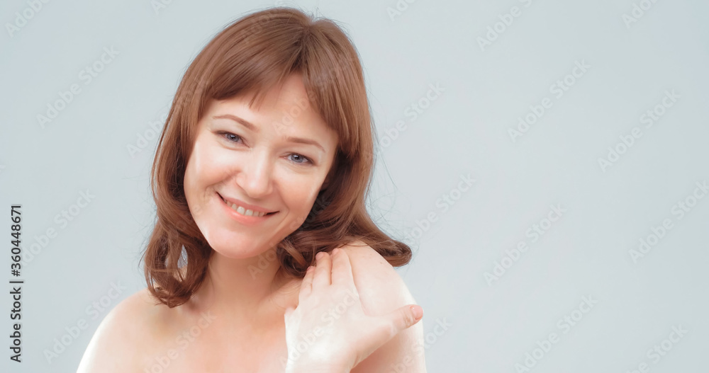 Mature brown-haired female applies skin care cream by touching face with hand, close up. Woman applying anti-age cream on her skin isolated on white background. Spa and wellness concept.