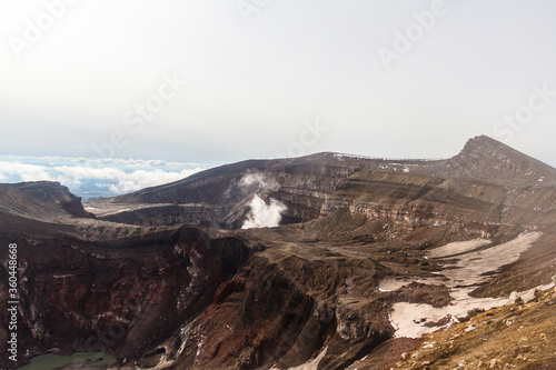 Daytime view of the mouth of an active volcano. Clouds on the horizon, mountains, volcanic lake are visible.