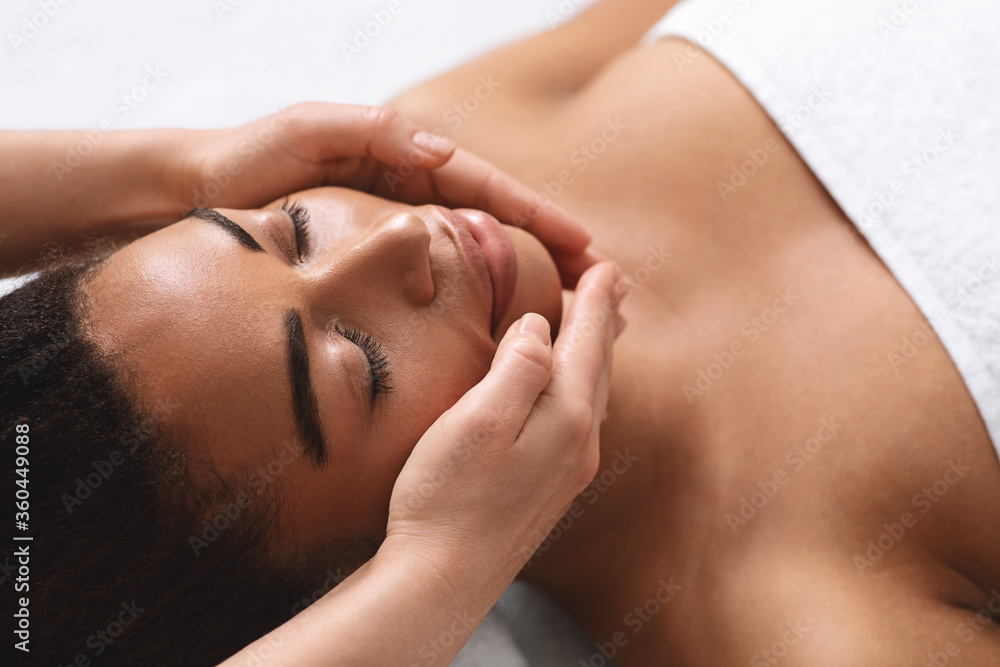 Closeup of therapist hands making facial massage for black lady Closeup of therapist hands making facial massage for black lady