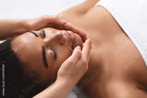 Closeup of therapist hands making facial massage for black lady